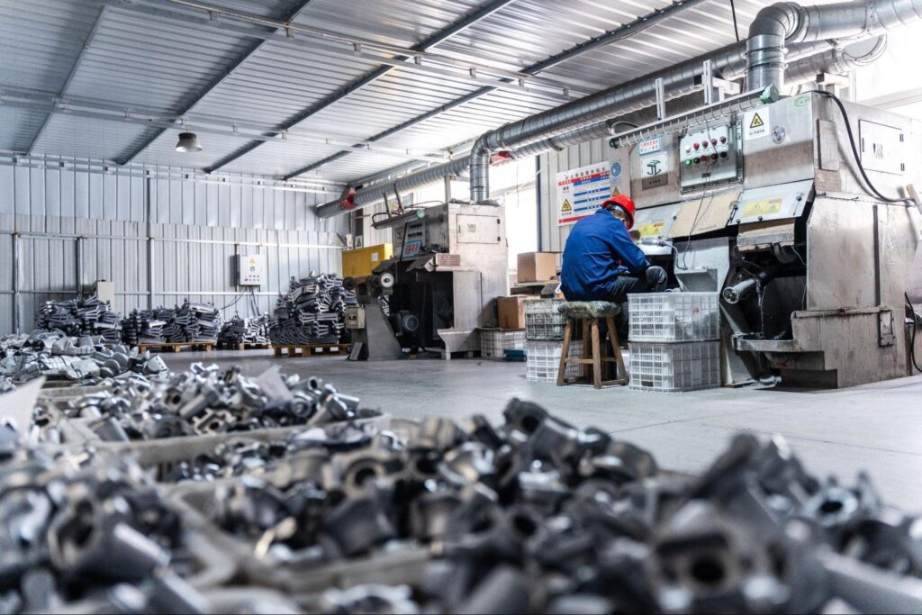 Factory interior with a worker sitting at a machine, surrounded by metal parts and industrial equipment