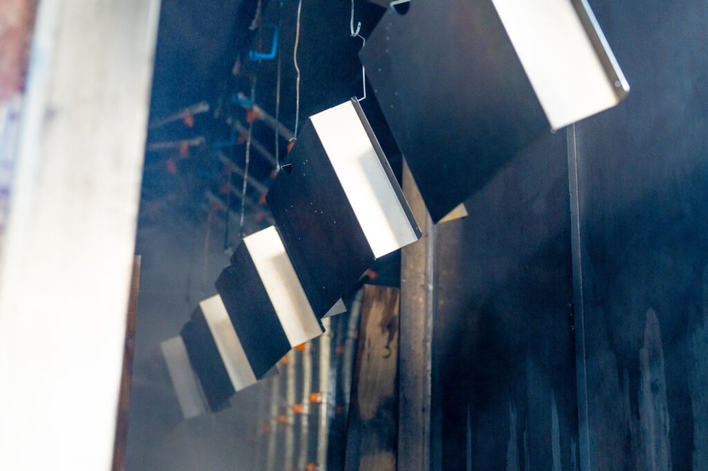 Close-up view of metal panels hanging on hooks inside an industrial coating or painting booth